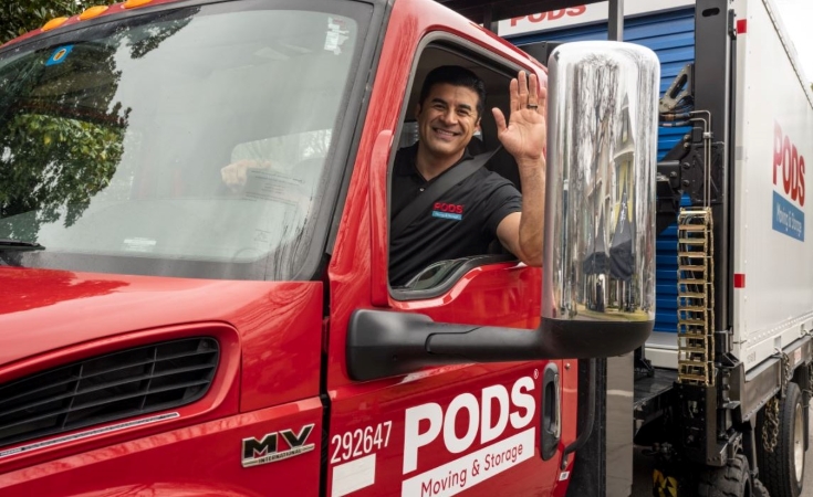 A PODS driver is smiling and waving from the cab of his truck. In the bed of the truck is a PODS portable moving container, ready to be transported to someone’s new home in Albuquerque, New Mexico.