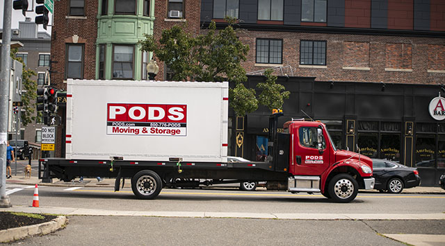 A PODS container being delivered on the back of a PODS Truck in the city