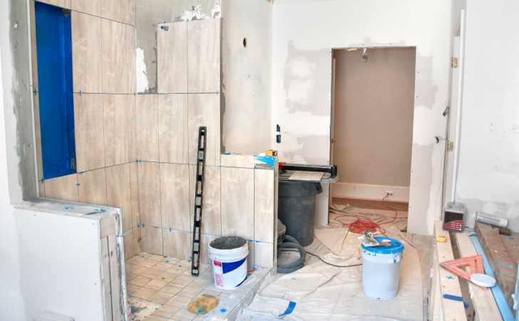  A primary bathroom is under construction. The shower has been partially dismantled, there are tools scattered around the room, and the walls are unfinished.