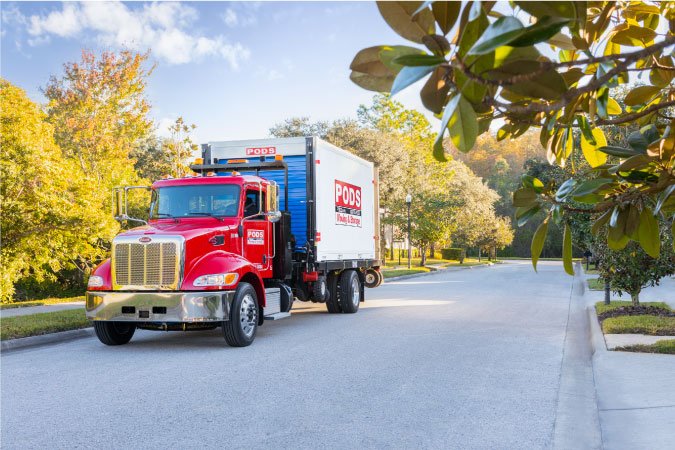 A PODS truck is transporting a portable moving container through a neighborhood in Charlotte, North Carolina.