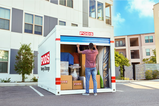 A young man is closing the sliding door on his fully-loaded PODS portable moving container