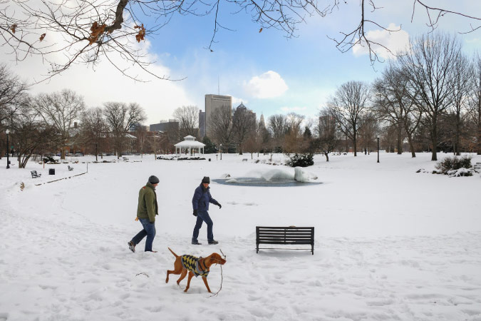 Two people and their dog are walking through a snowy park in Columbus, Ohio