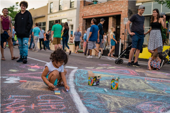 A little girl uses sidewalk chalk to decorate a pedestrian street on a sunny day in Denver’s Art District on Santa Fe.