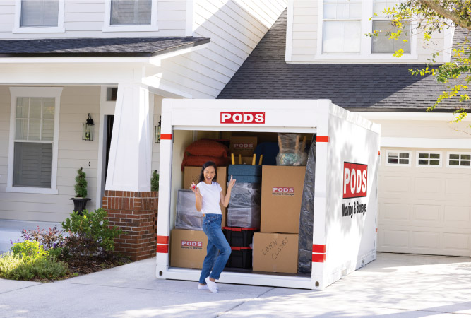 A woman poses excitedly for a photo in front of her loaded PODS container, which is sitting in her driveway.