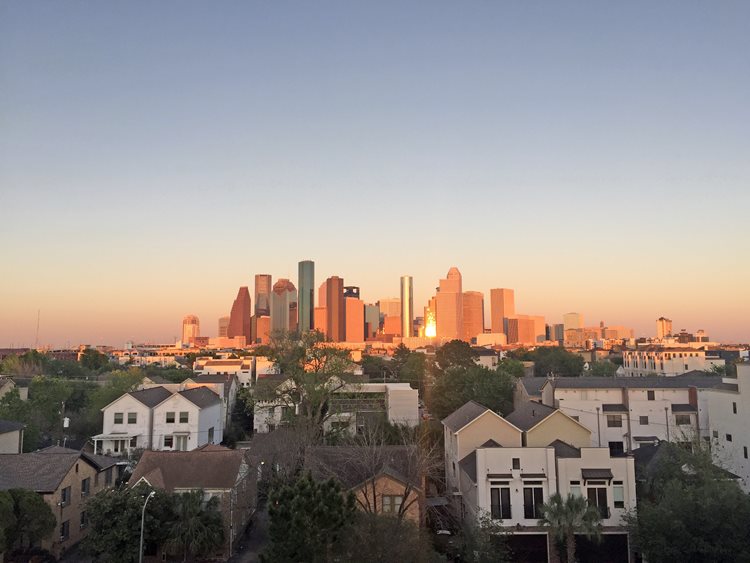 White and cream townhomes in Houston, Texas, with the skyline of the city in the background and the light reflecting off the buildings. 