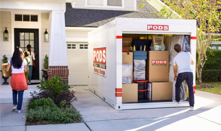 A family of four is working together to unload their things from the ӰPro portable moving container in their driveway.