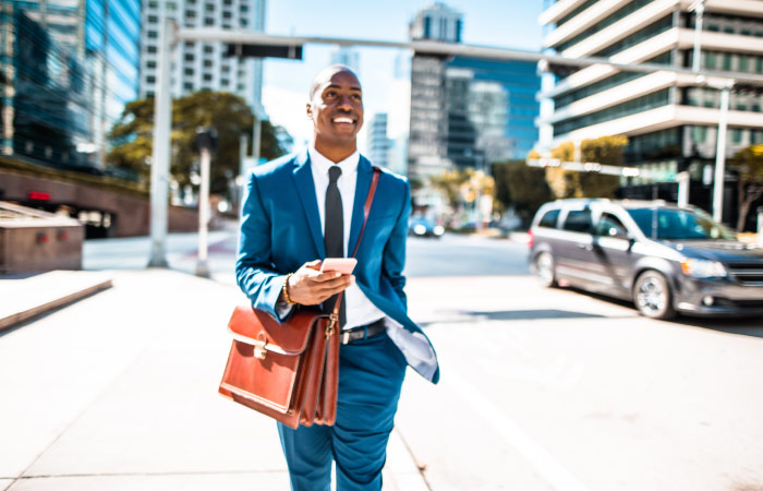 A man in a professional business suit is smiling as he walks through Downtown Miami on his way to work.