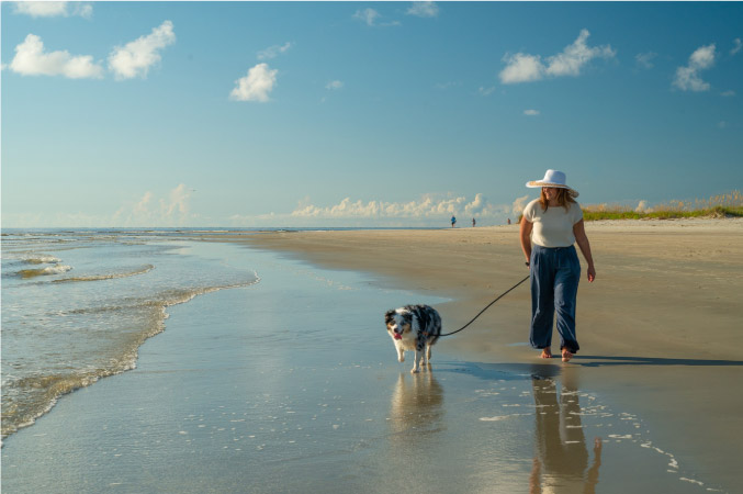 A young woman is walking her dog at the beach on St. Simons Island in the late afternoon.