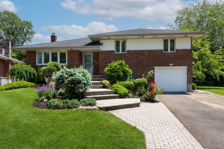 A residential home in Jericho, New York — one of the top New York suburbs. The house has two stories and features a mostly brick exterior and a beautifully landscaped front yard.