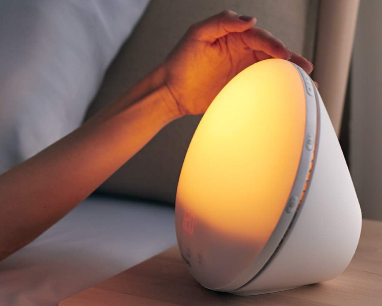 Close-up of a woman’s arm touching the top of her Sunrise Alarm Clock, which is on top of her nightstand.