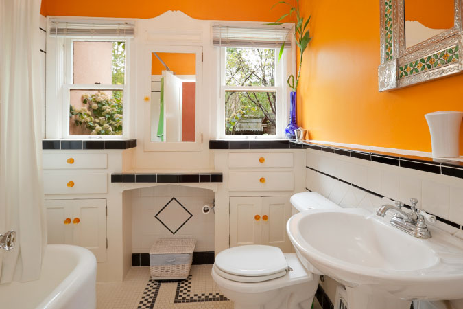 A newly remodeled bathroom with black and white tiles and cabinets, orange accent handles, and matching orange walls. 