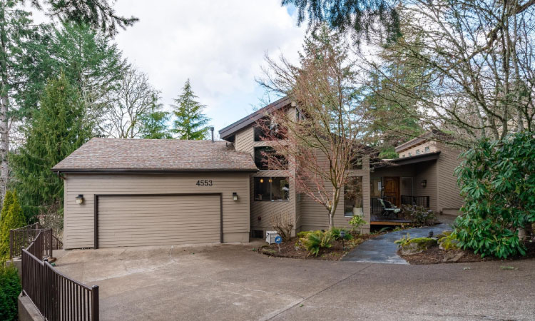 A large tan-colored residential home in the woods of Salem, Oregon, featuring an asymmetrical exterior, a large driveway, and a covered porch.