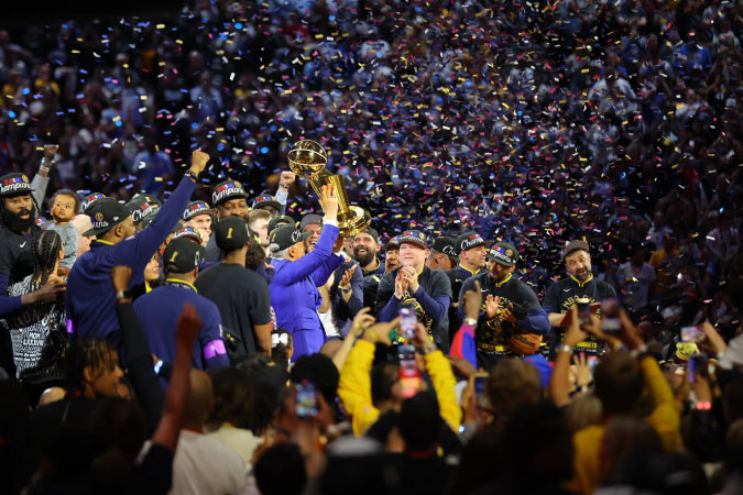 The Denver Nuggets celebrate their championship win in 2023 with their fans as confetti falls from the arena ceiling.
