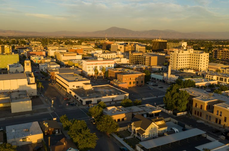 Sunset view of Bakersfield, California, with the city buildings reflecting the yellow light of the sun and the mountains and some of the Bakersfield neighborhoods visible in the distance.