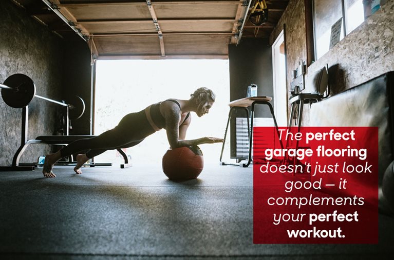 A woman is wearing exercise clothes while doing a plank workout on an exercise ball in her home garage gym. There are weights in the corner, the garage door is open, and light is reflecting off the garage gym flooring. There is a red square on the right side of the image with overlaid text that reads “The perfect garage flooring doesn't just look good — it complements your perfect workout.”