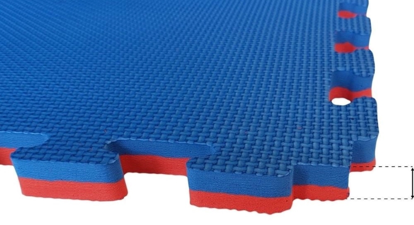 A close-up view of the corner of a blue and red foam floor mat with interlocking cutouts for connecting to other foam mat pieces. Graphic lines on the side of the image emphasize how thick the mat is.