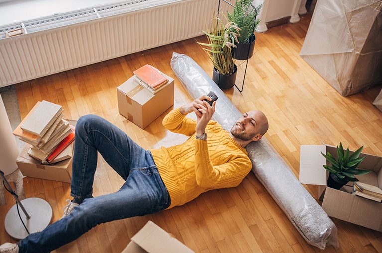 A man reads his phone, laying on a rolled-up carpet.