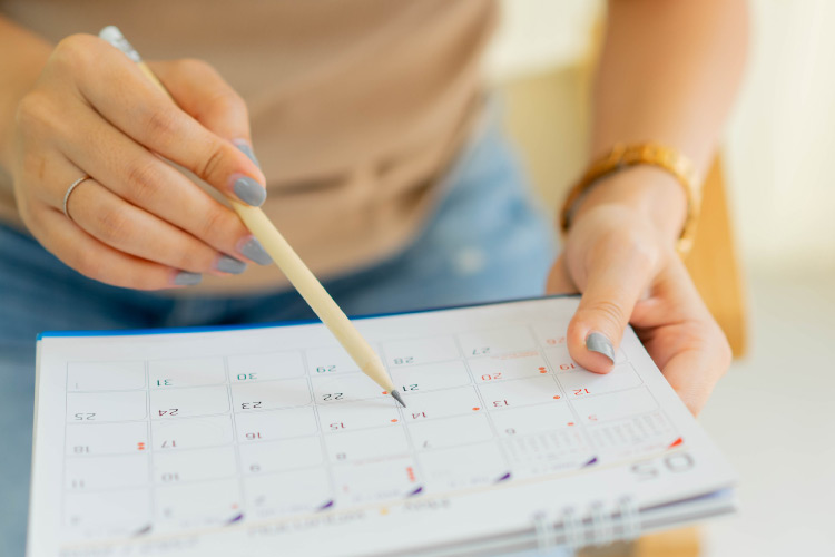 A woman is holding a calendar and using a pencil to mark key dates as she plans her upcoming move. 