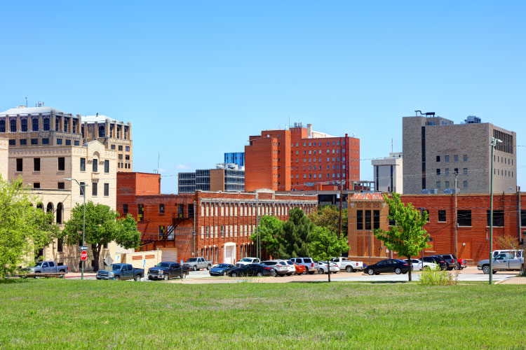 The skyline of Wichita Falls, Texas, on a sunny day, seen from across an expansive lawn. The downtown buildings are mostly made of brick and vary in colors from red to cream.