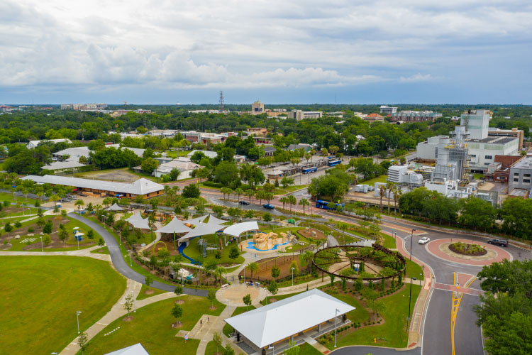 Aerial view of Gainesville, Florida, featuring a community park in the foreground and city buildings interspersed with woodlands in the distance.
