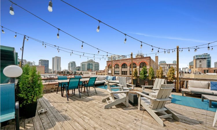 A rooftop view in Chicago’s River North neighborhood. The deck is made of wood and several sets of outdoor patio furniture are set up, creating a pleasant spot to enjoy the lovely weather. There are also outdoor lights strung back and forth above the deck, so it can be enjoyed even at night.