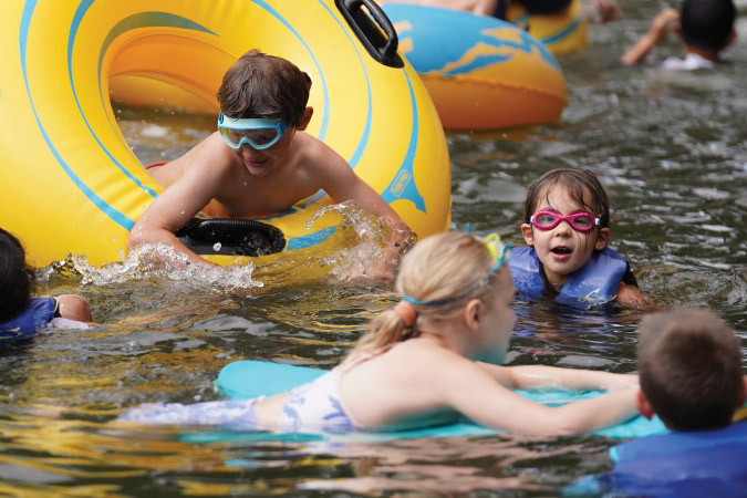 Young kids decked out in swimsuits, goggles, and life jackets enjoy a summer day swimming in Lake Oswego, Oregon — one of the best Portland suburbs.