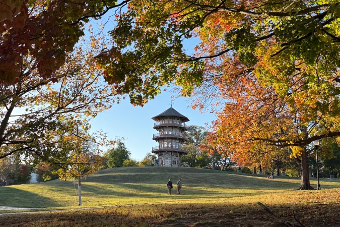 A couple is walking across a vast lawn in Patterson Park toward the pagoda on an autumn afternoon