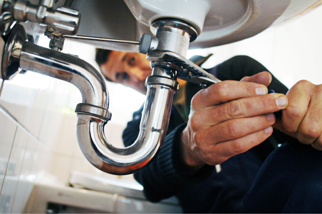 Close-up of a plumber tightening a pipe under a residential bathroom sink during a bathroom renovation