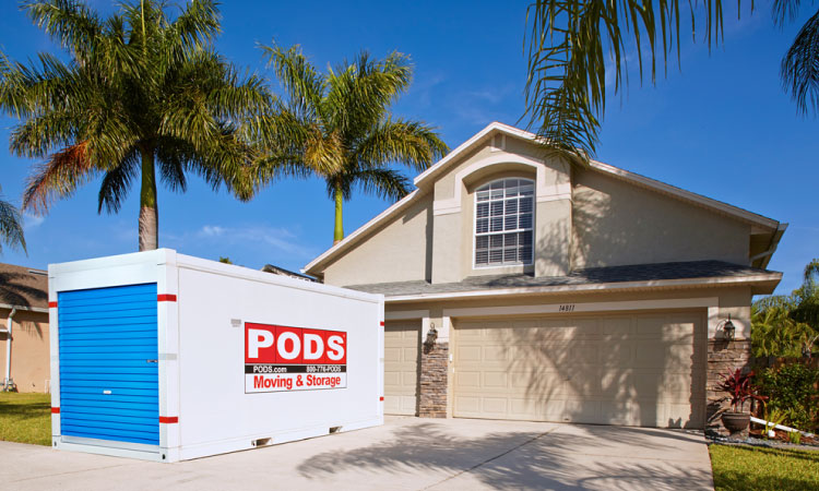 A two-story, stucco-exterior home in Florida with palm trees in the yard and a PODS portable moving and storage container sitting in the driveway.