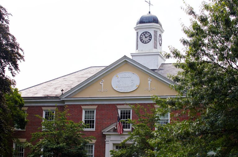 Exterior view of City Hall in Rye, New York. The building is made of red brick and features a prominent front-facing gable and a clock tower. 