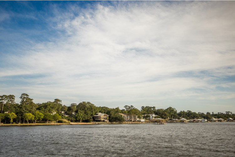 View of waterfront homes in Fairhope, Alabama, on a sunny day. Some of the homes are built on stilts, and many of them have docks jutting out into the water.