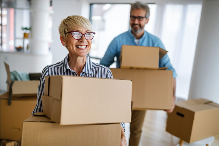 A happy mature couple is carrying moving boxes out of their house, in preparation for their retirement to Alabama.