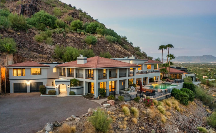 A luxury mansion in the hills of Paradise Valley, Arizona. The home features a large wrap-around porch on the second level, an outdoor pool, a two-car garage, and incredible views of the valley below.