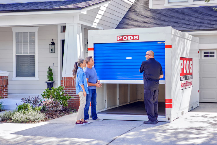 A retired couple speaks with a PODS driver as he opens the door to the PODS portable moving container in their driveway. 