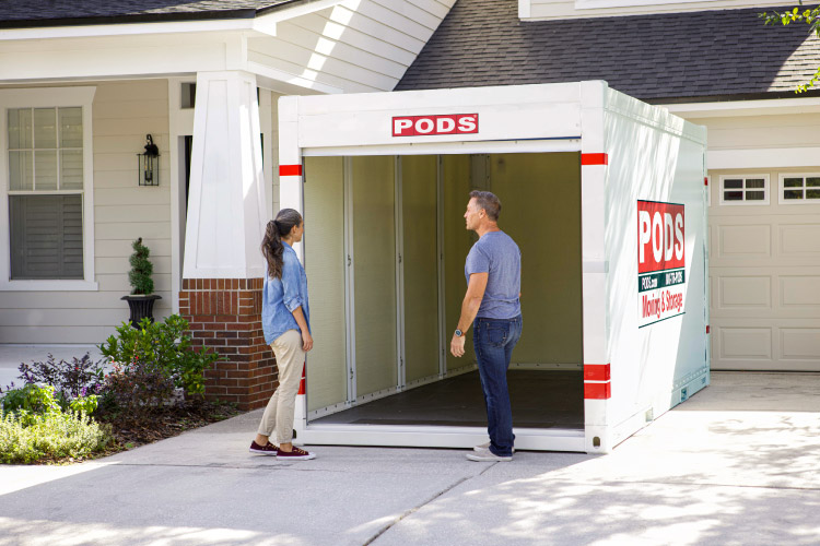 A recently retired couple inspects the empty PODS portable moving container in their driveway. The door of the container is open and the container is ready to be loaded.