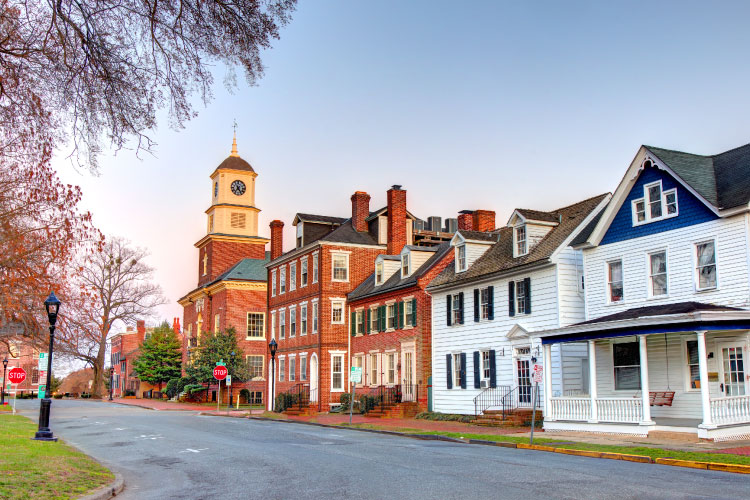Buildings in downtown Dover, Delaware, just before dusk. Most of the buildings are made of red brick, but the two in the foreground feature a white siding exterior.