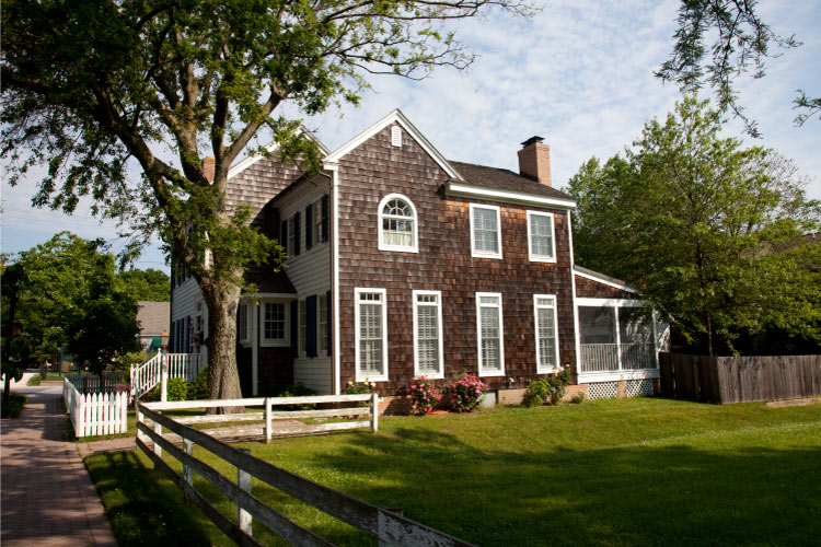A residential property in a historic part of Lewes, Delaware. The two-story home features a wood shingle exterior and a fenced-in lawn.