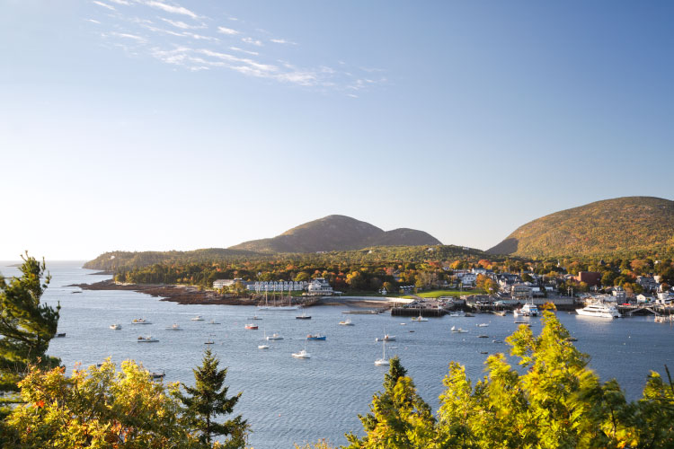 A view of the coast along Bar Harbor, Maine, from across the water. Resorts and marinas line the waterfront as mountains rise up behind the town.