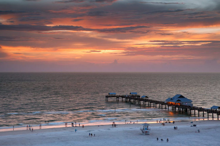 View of Clearwater Beach and Pier 60 at sunset. Several people are enjoying the sunset on the sugar-sand beach and along the pier.