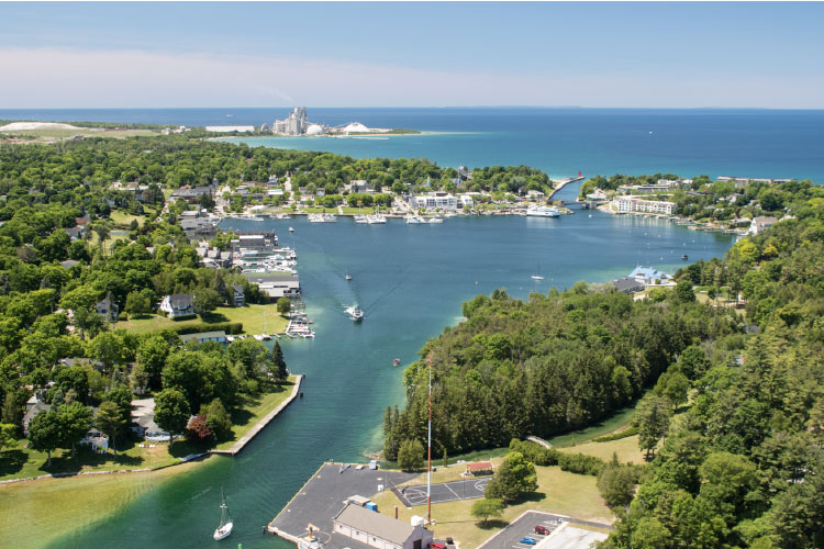 Aerial view of waterfront properties in Charlevoix Township, Michigan. Boats are moving along the waterway past wooded neighborhoods. 