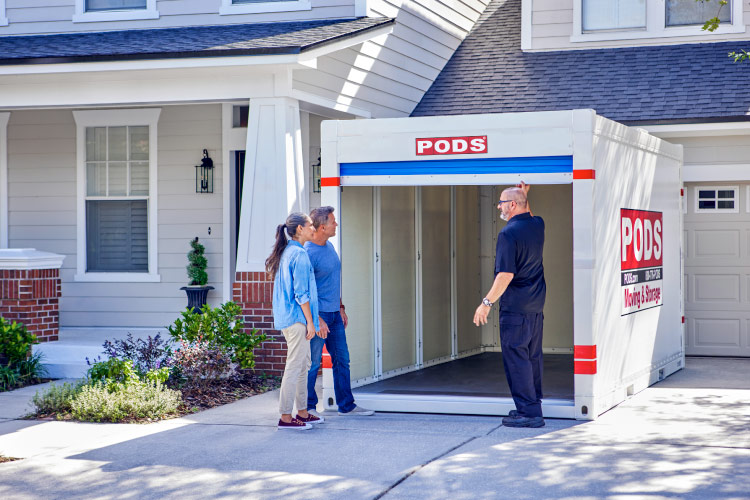 A senior couple is checking out the PODS portable moving container in their driveway as a PODS driver opens the door to the container. 