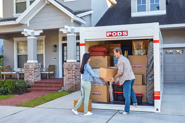 A retired couple is loading their PODS portable container with moving boxes. The container is nearly full, already expertly loaded with boxes and furniture.