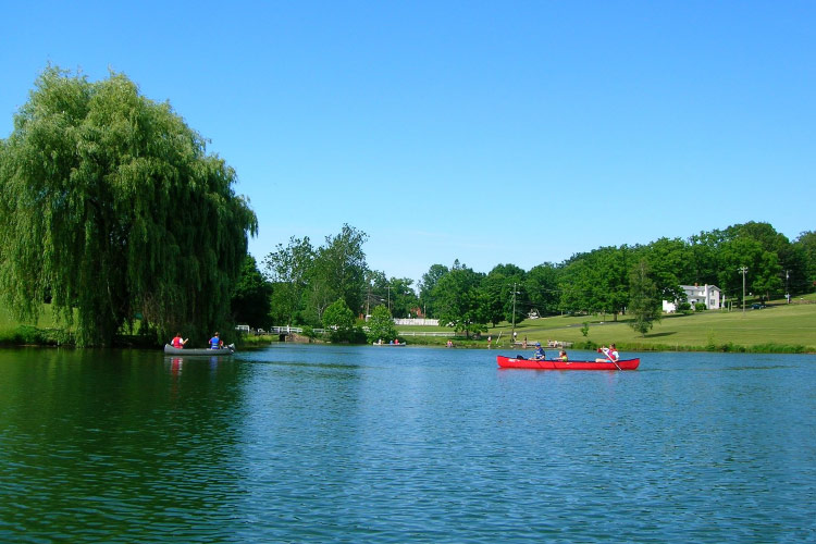 Residents canoe on a body of water in Massanetta Springs, Virginia. It’s summer,  the grass is green, and the trees in the community are filled with lush foliage. 