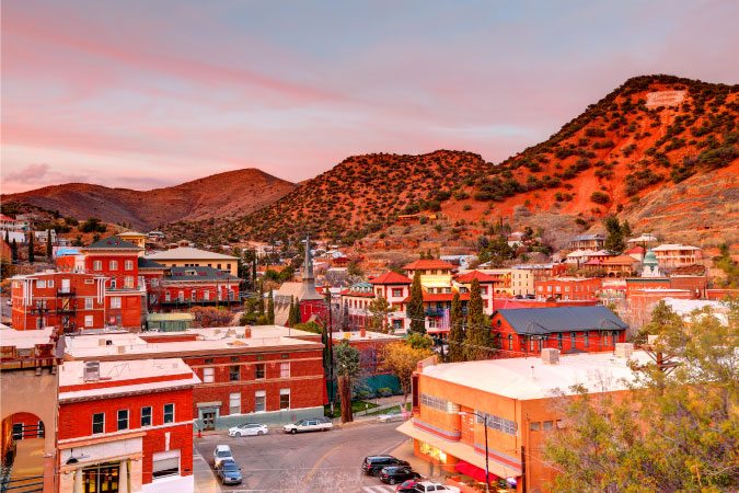 A rooftop sunset view of Bisbee, Arizona, featuring red brick buildings and the surrounding hills.