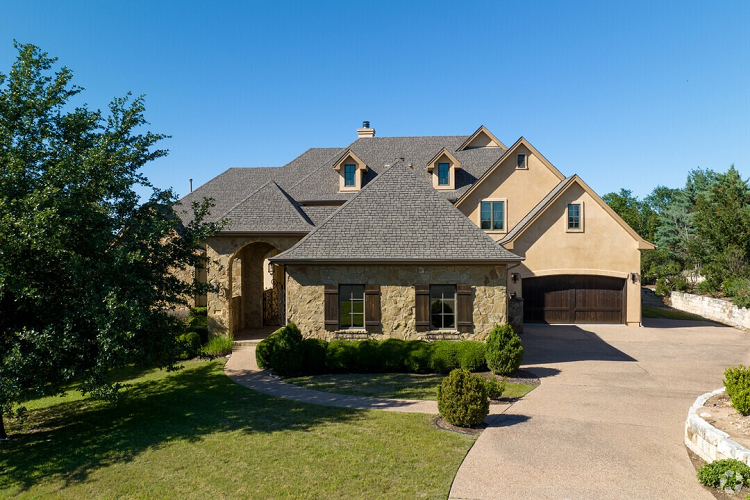 Exterior view of a large mansion in Austin’s East Oak Hill neighborhood, featuring a large, two-car garage, stone facade, and a tall, covered entrance.