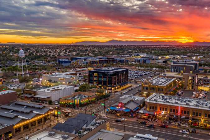 Aerial view of the Phoenix suburb of Gilbert during a stunning sunset, with orange and yellow hues staining the sky above the city