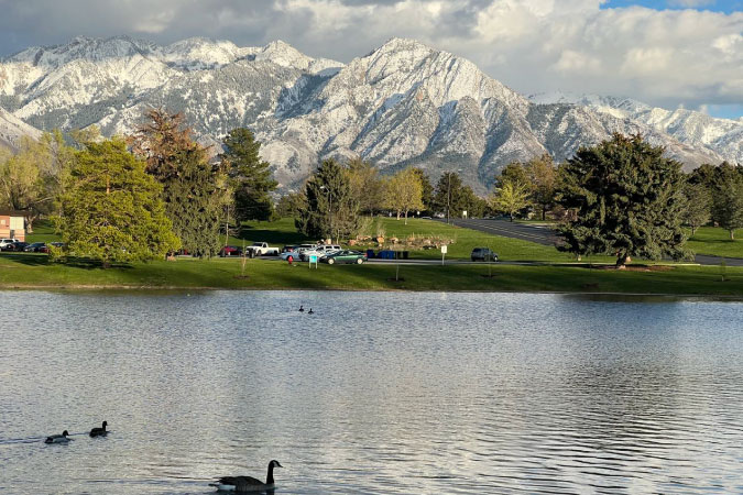 Canadian geese float atop a lake with a snowy mountain backdrop in Sugar House Park, a popular green space in the Sugar House neighborhood of Salt Lake City. 