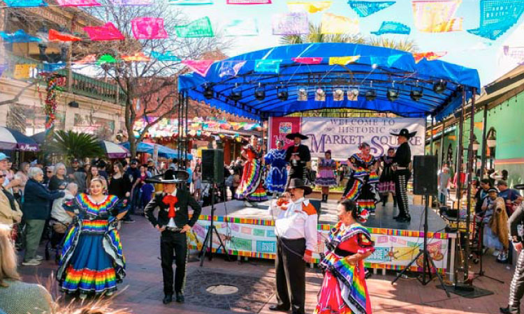 Music and dancing at Historic Market Square in San Antonio on a beautiful spring day. Women and men in traditional costumes are performing on stage as locals enjoy the show.