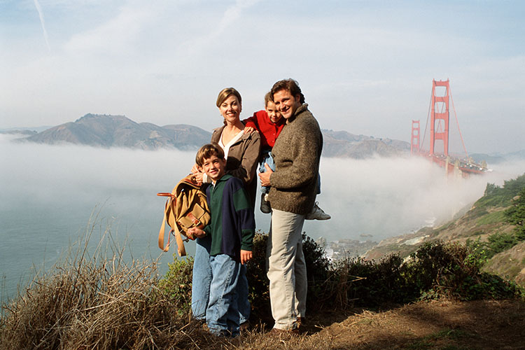A happy family of four poses for a photo on a hill overlooking the Golden Gate Bridge as fog rolls in over San Francisco.