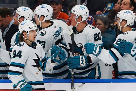 The San Jose Sharks NHL team celebrates a goal in their white jerseys with teal accents. 